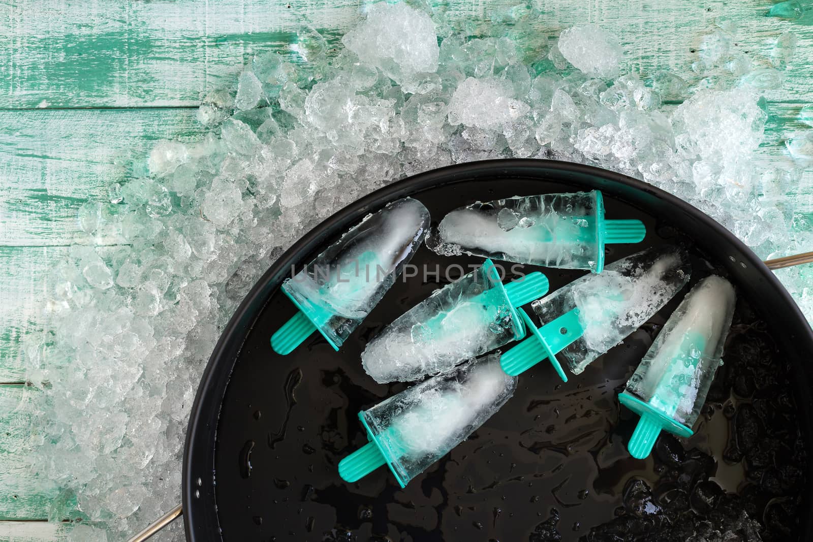 Ice crushed on green wooden background and ice in a black tray by kaiskynet