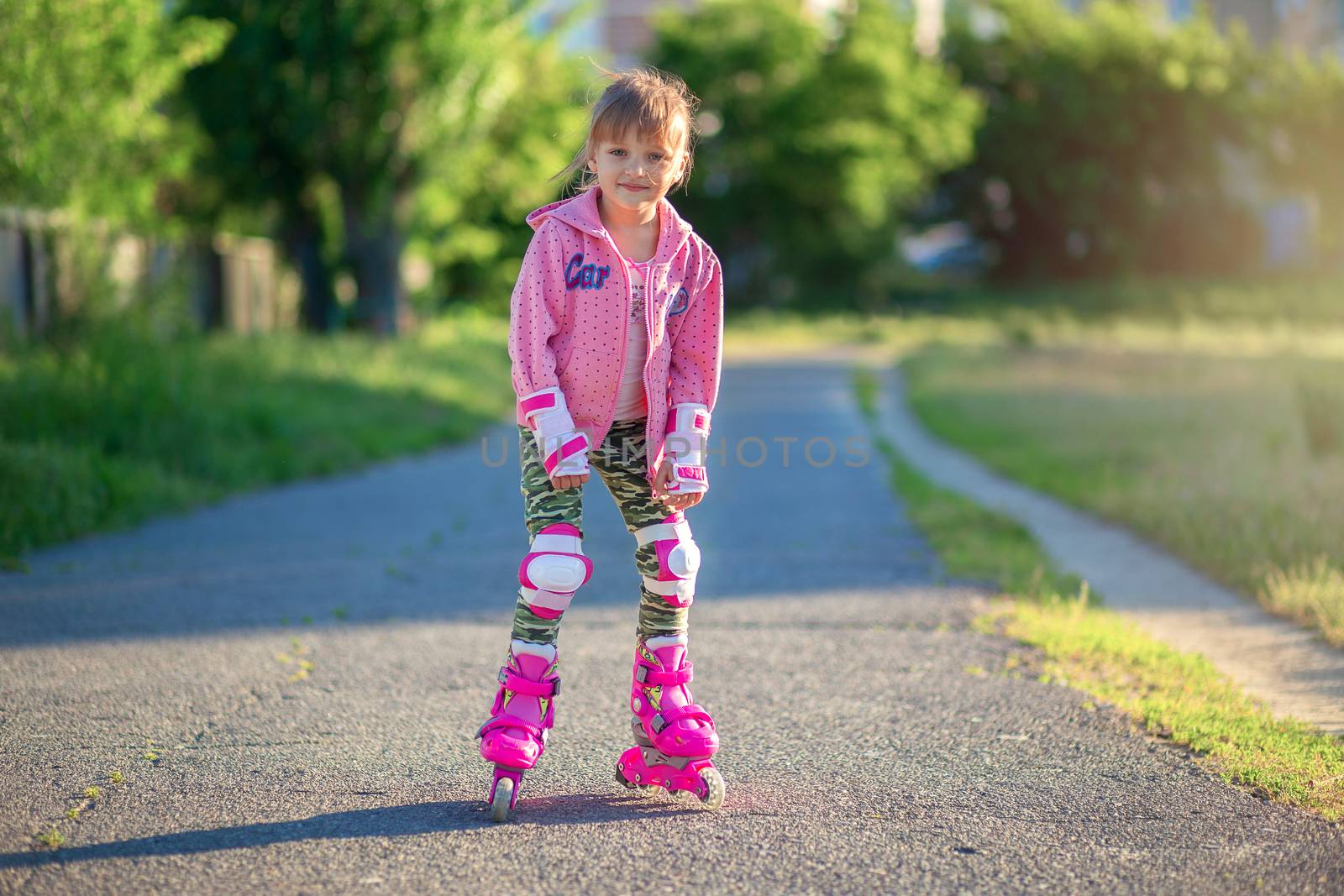 Little girl in pink rollers and pink sweater posing in the park and smiling. Happy child rollerblading. Children's sports and healthy lifestyle