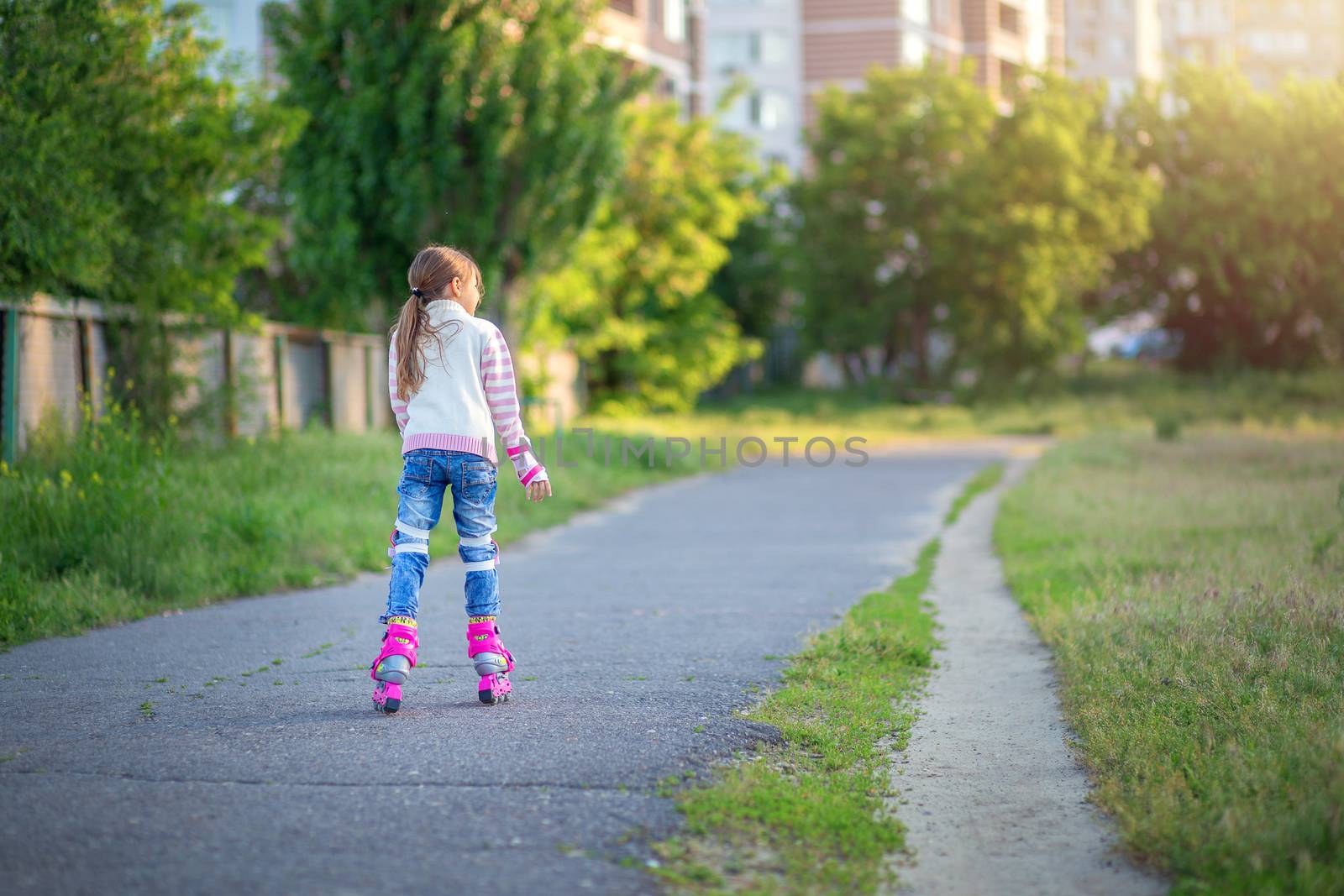 A little girl rides on pink roller skates on asphalt in the summer. The child learns to ride roller skates. Skating. Children's sports and healthy lifestyle