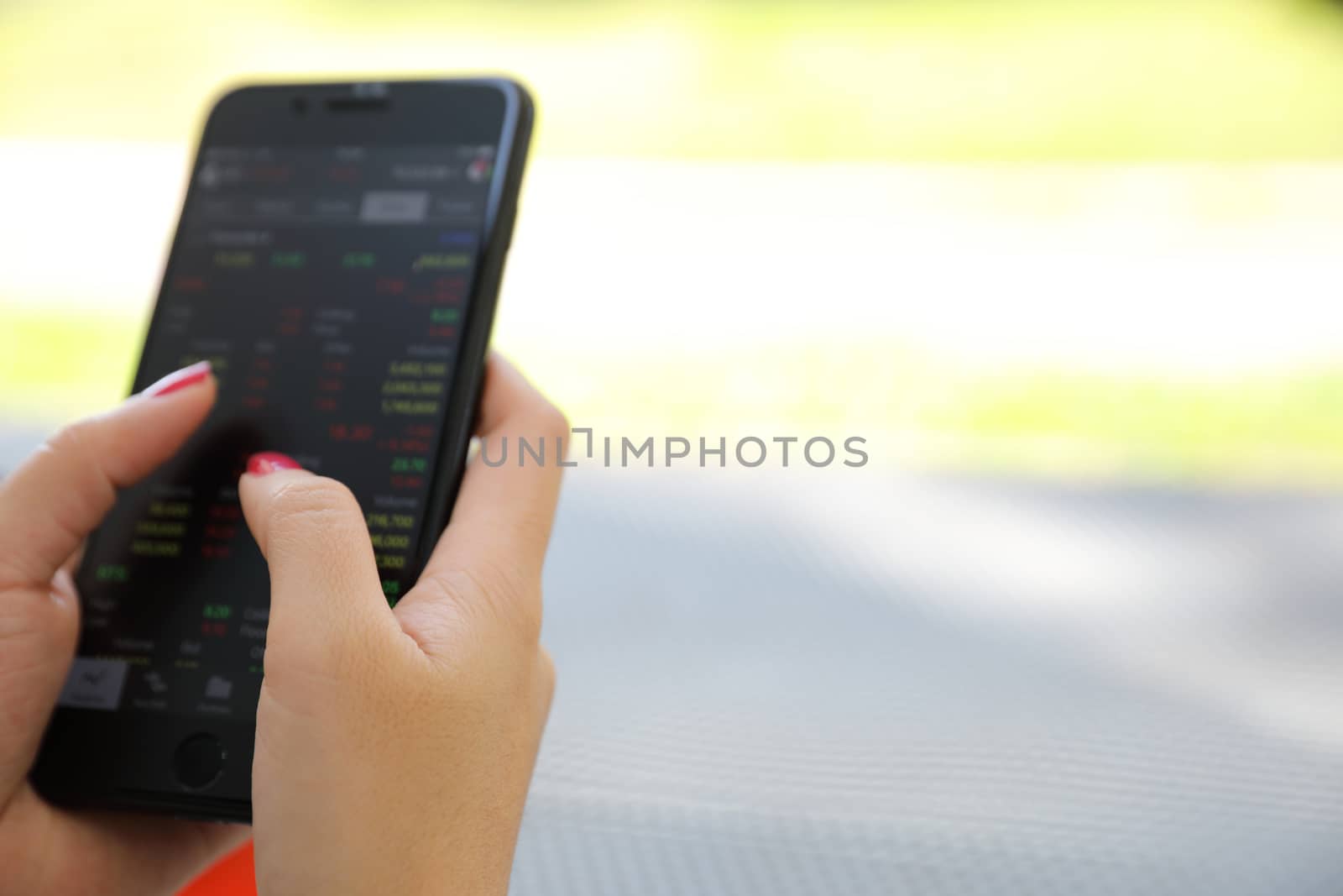 Female hand with smartphone trading stock online in coffee shop  by piyato