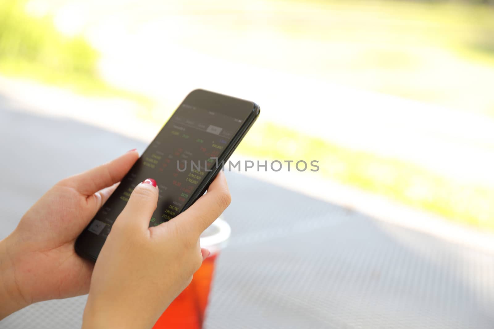 Female hand with smartphone trading stock online in coffee shop  by piyato