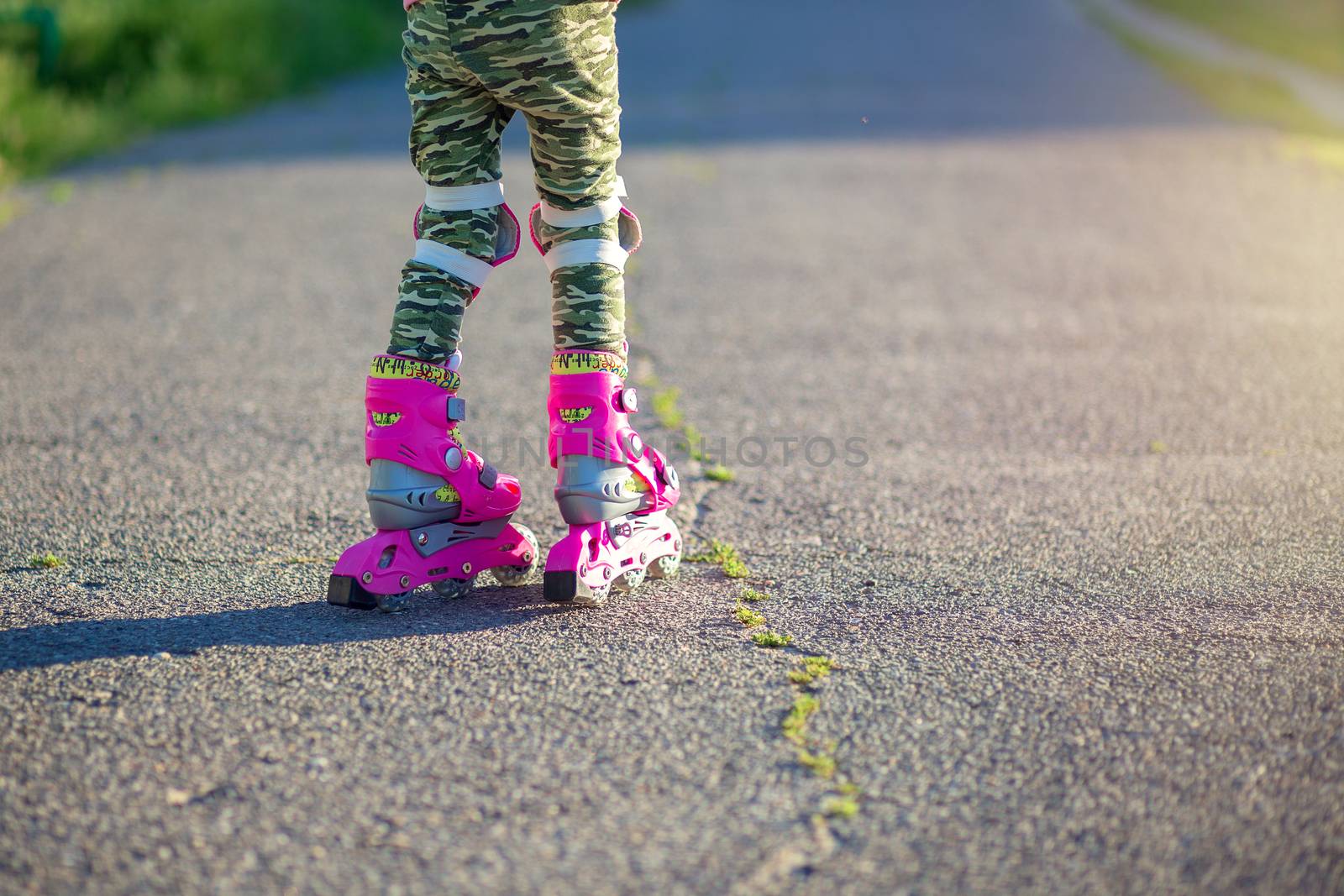 A little girl rides on pink roller skates on asphalt in the summer. The child learns to ride roller skates. Skating