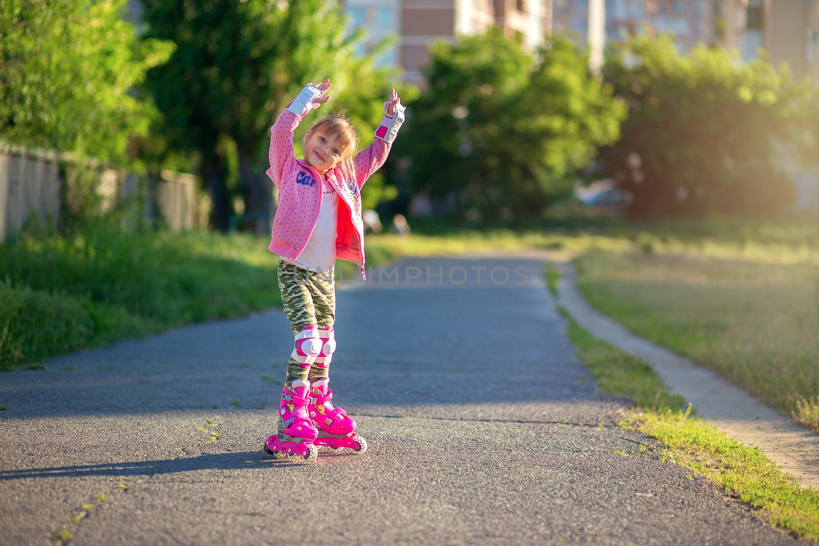 Little girl in pink rollers and pink sweater posing in the park and smiling. Happy child rollerblading. Children's sports and healthy lifestyle