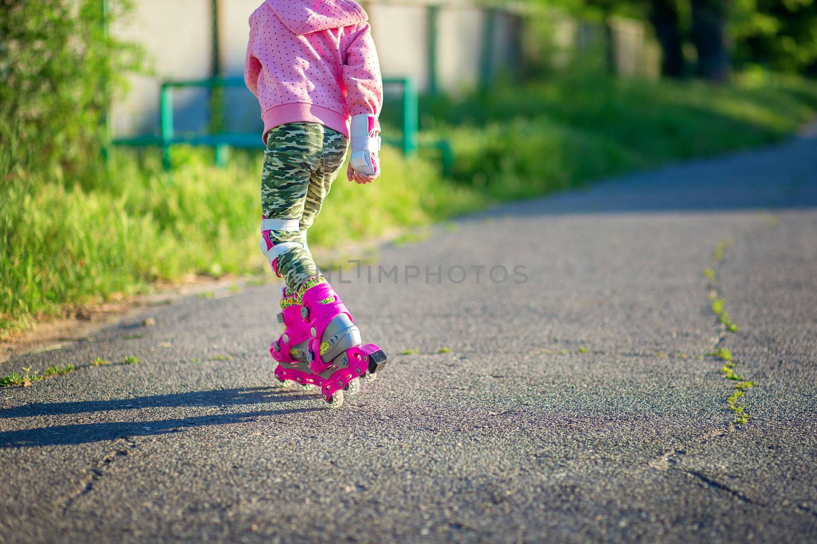 A little girl rides on pink roller skates on asphalt in the summer. The child learns to ride roller skates. Skating