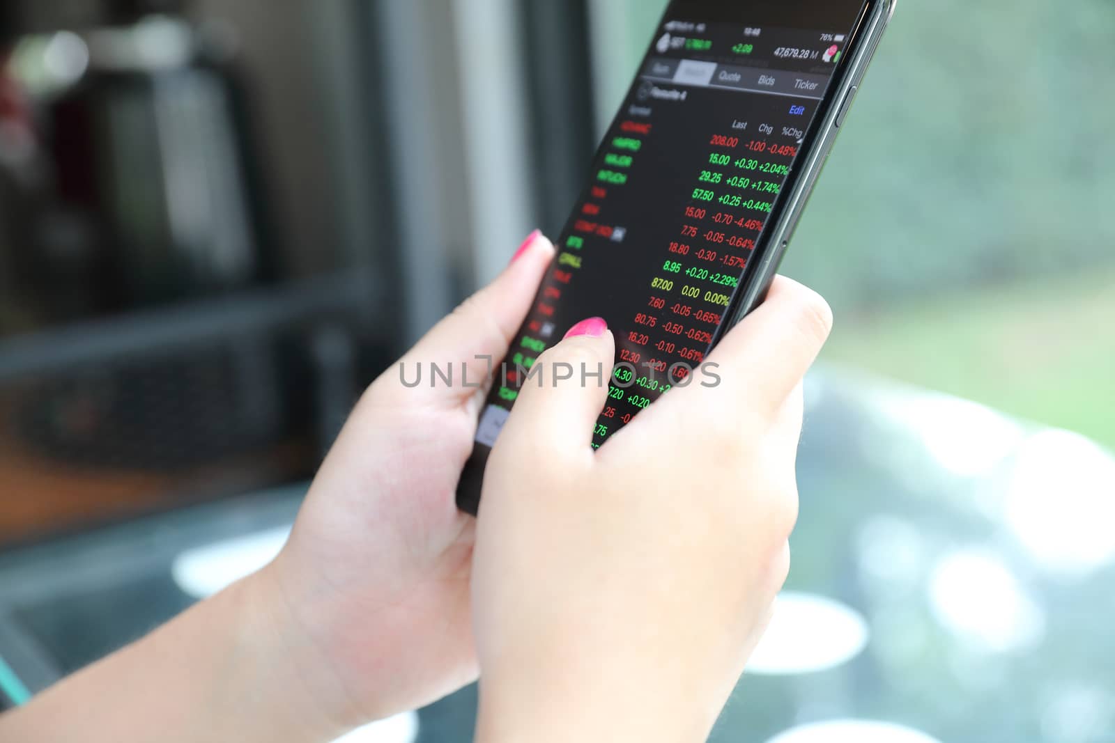 Female hand with smartphone trading stock online in coffee shop , Business concept