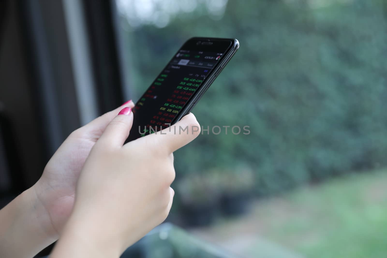 Female hand with smartphone trading stock online in coffee shop  by piyato