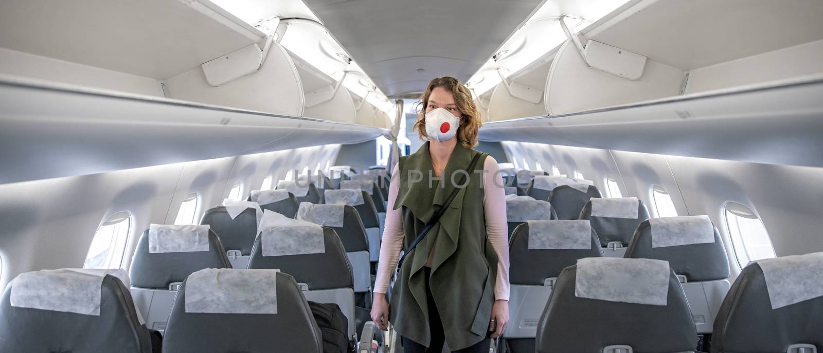 woman on board of aircraft with respirator on head. protect themselves against viral disease. People cancel travel abroad due to coronavirus by Edophoto