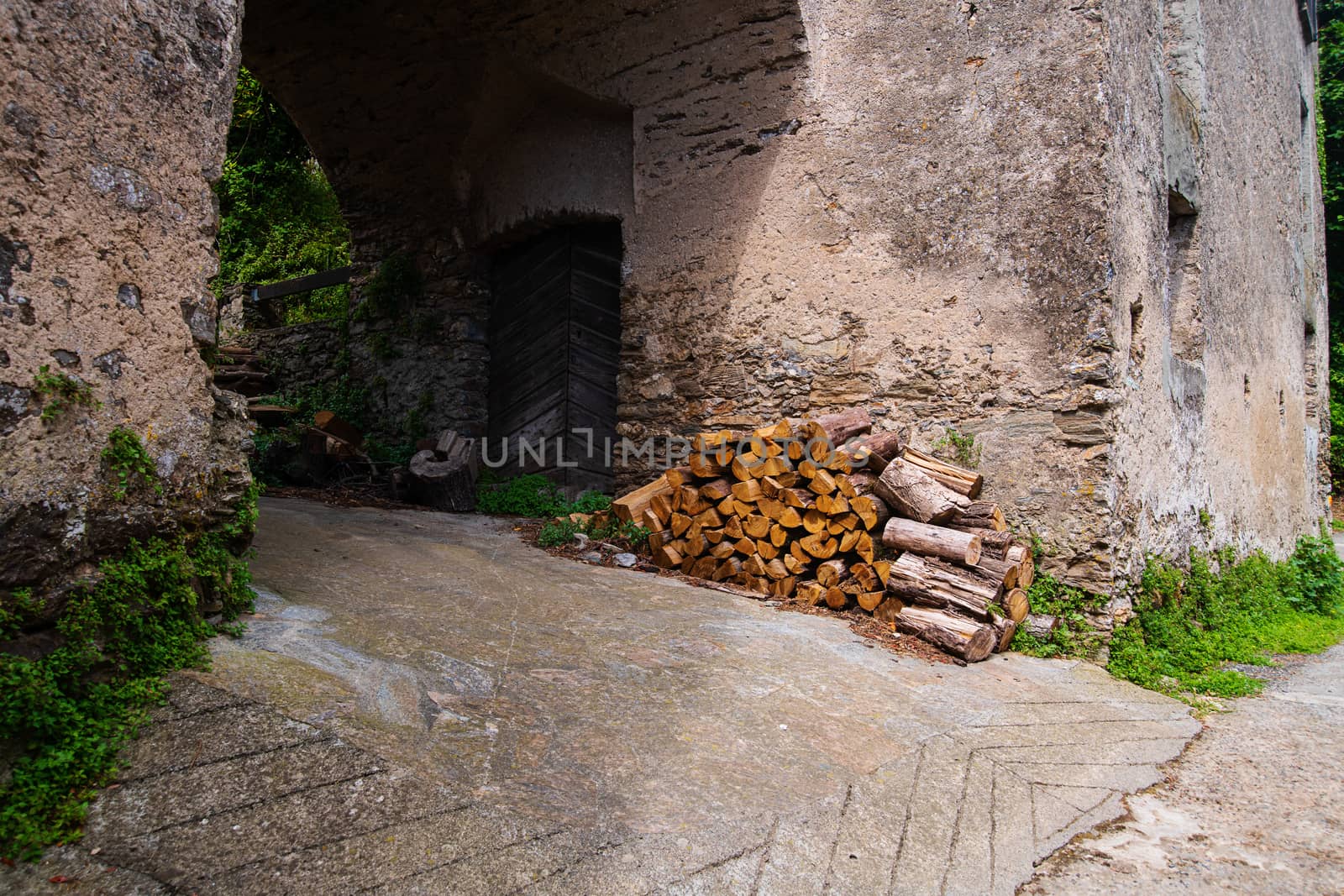 a pile of wood against the wall of an old house with a trespassing with a wooden door on the isle of Corsica in France during summertime