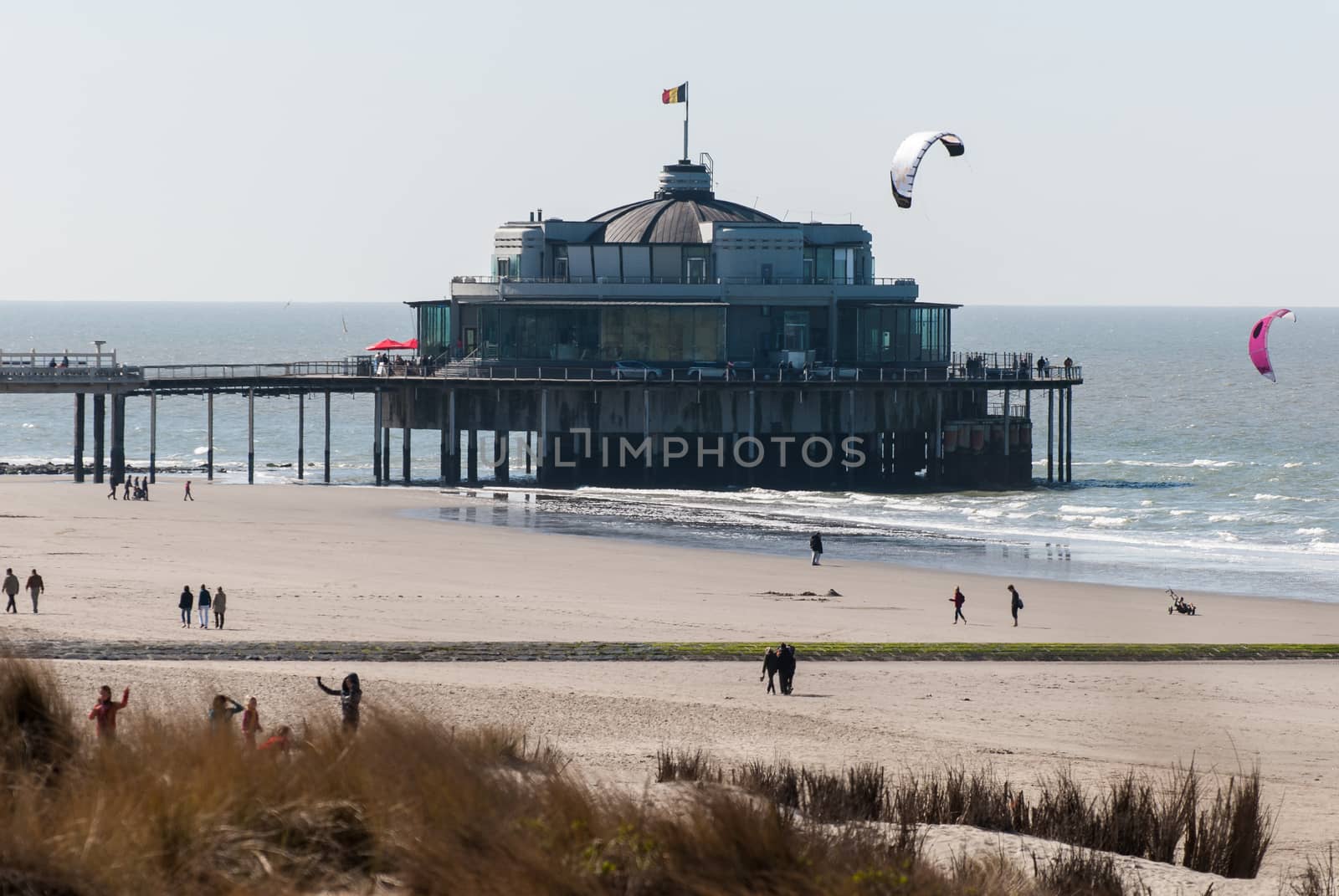 view on the jetty of Blankenberge at springtime with some kitesurfers around an people walking on the beach