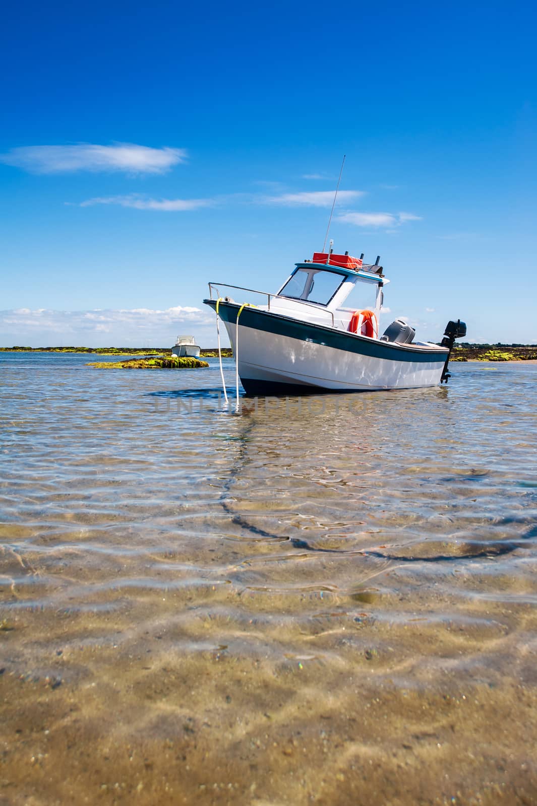 White boat on sand surrounded with water and rocks in summertime in Noirmoutier