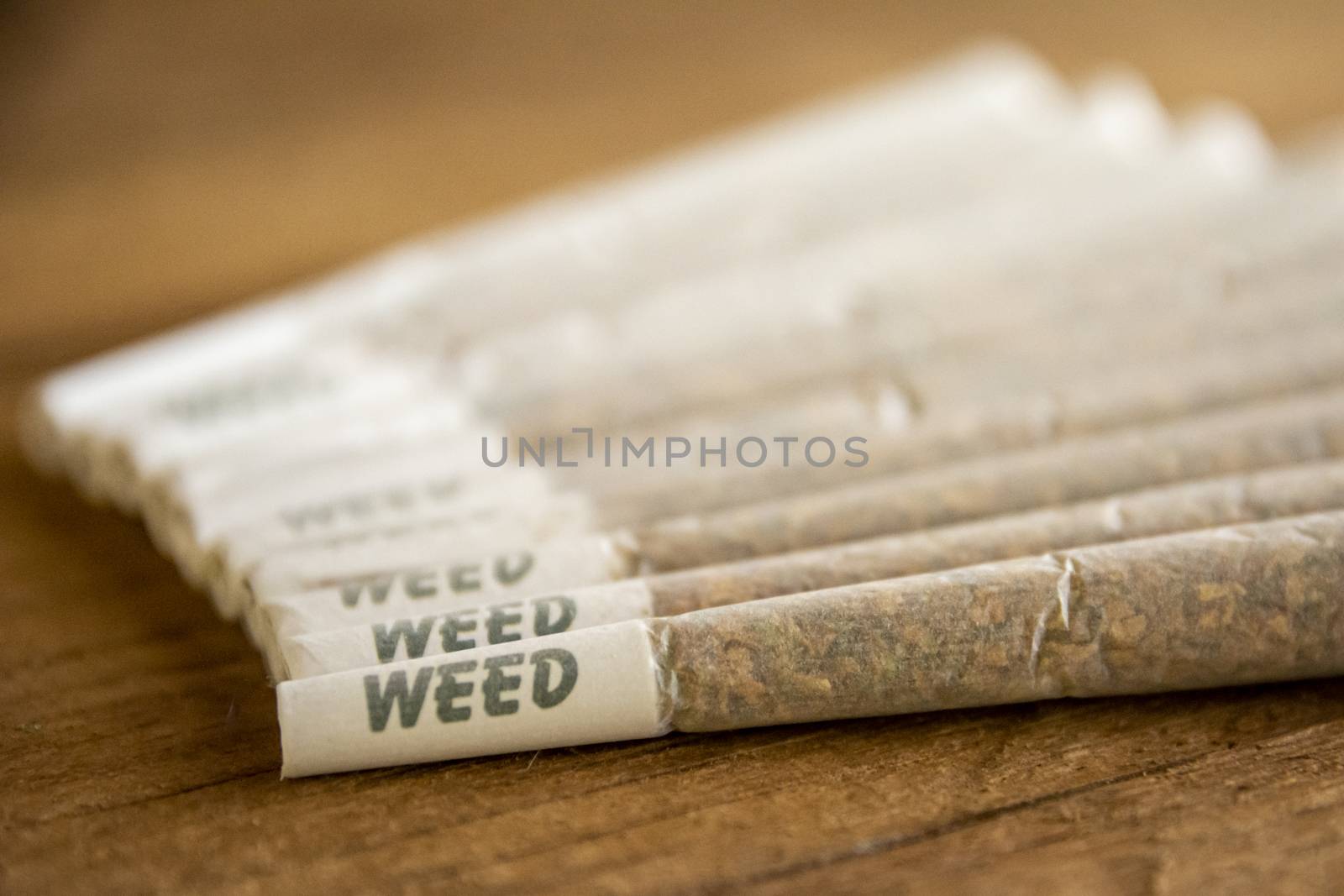 A bunch of Dutch Marijuana or weed joints next to each other, lined up, on rough wood, warm sunlight from the side.