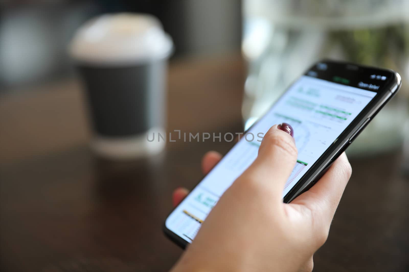 Female hand with smartphone trading stock online in coffee shop  by piyato