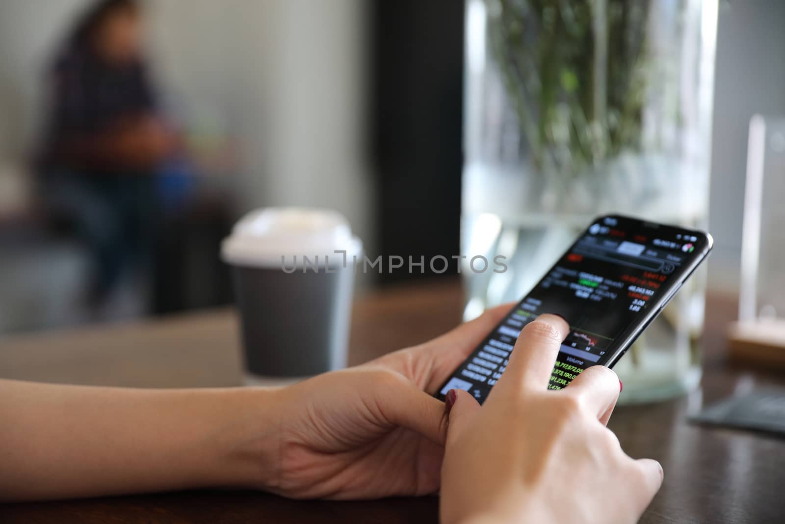 Female hand with smartphone trading stock online in coffee shop , Business concept