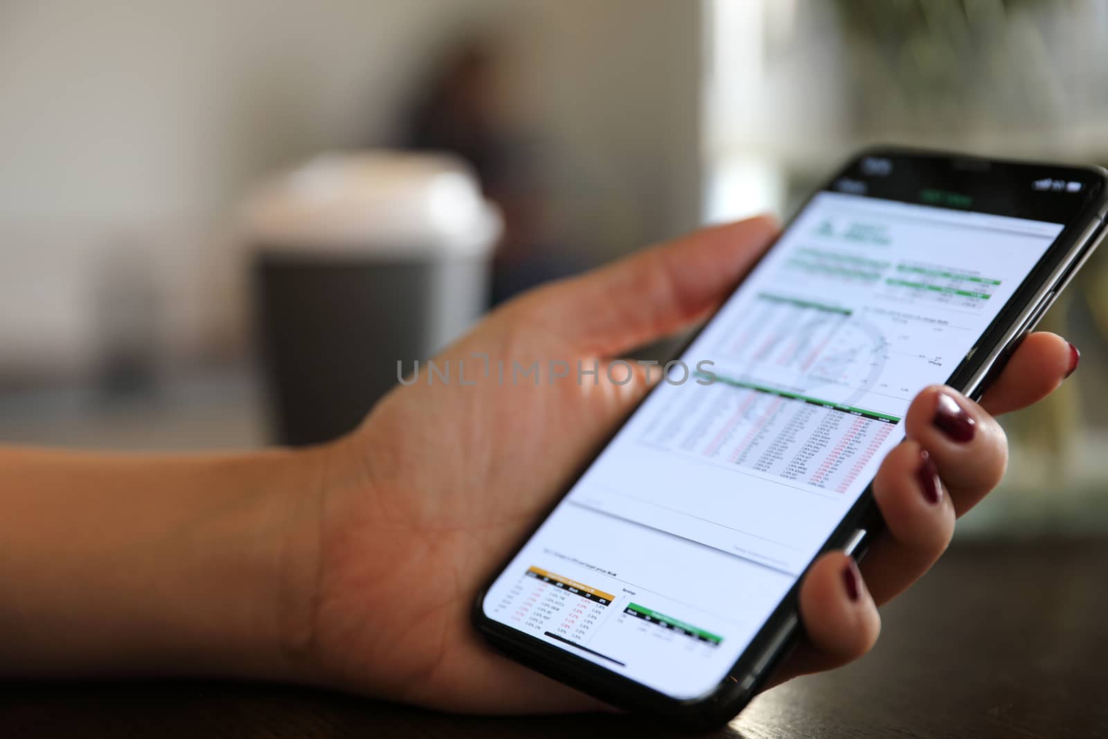 Female hand with smartphone trading stock online in coffee shop , Business concept