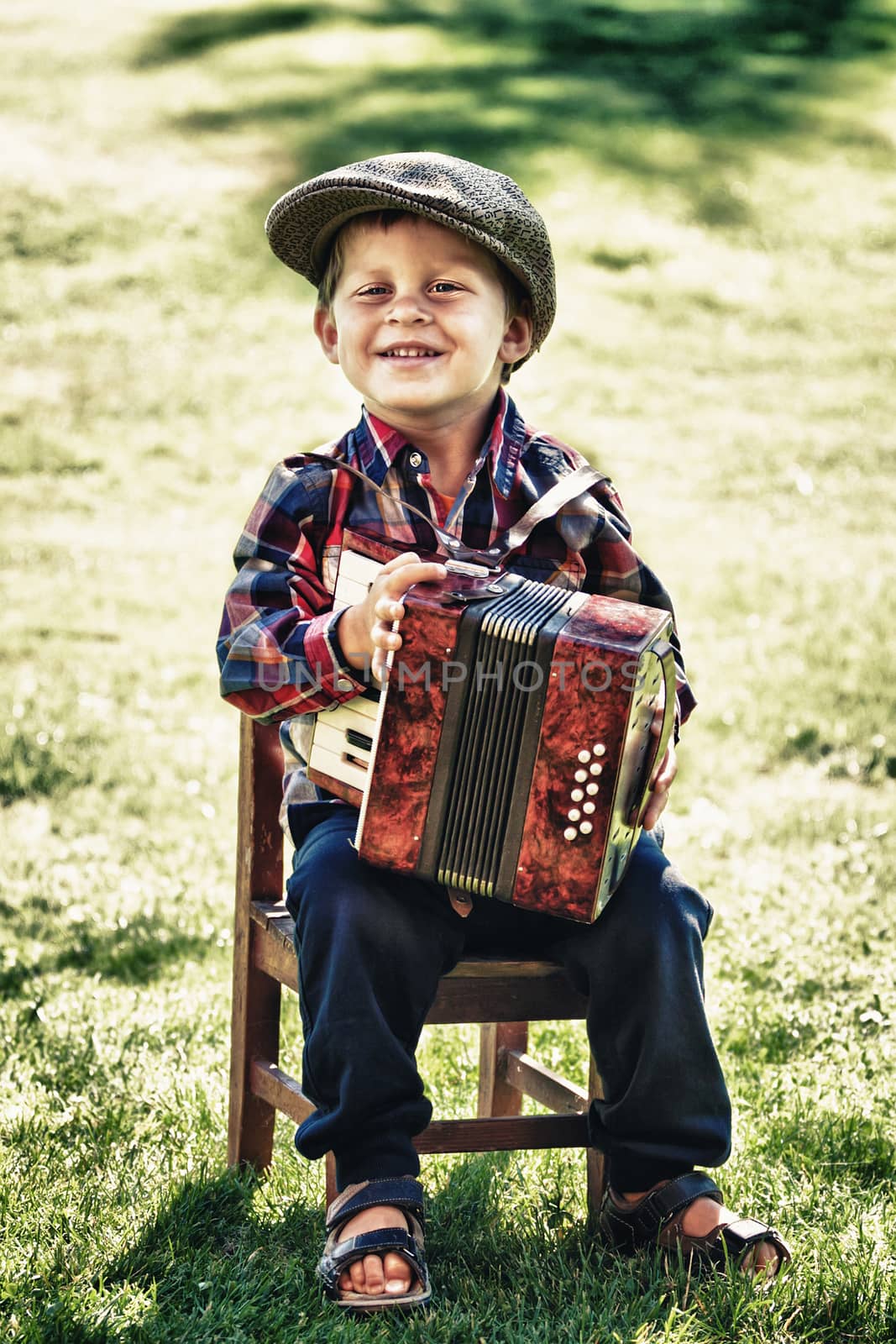 happy young boy playing accordion in summer 