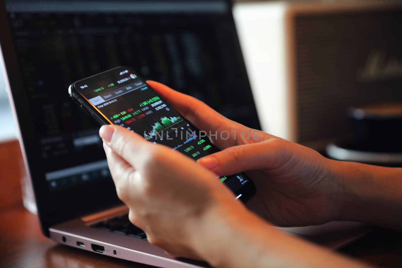 Female hand with smartphone trading stock online in coffee shop  by piyato