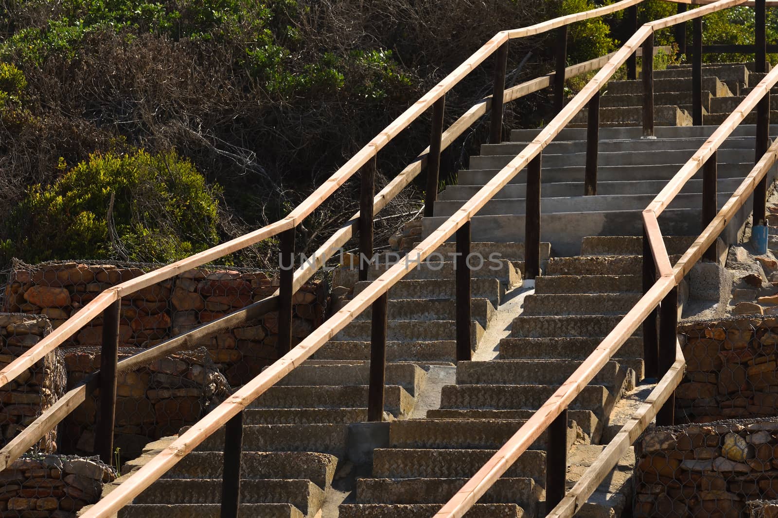 A beach exit cast concrete staircase with wooden handrails going uphill, Mossel Bay, South Africa