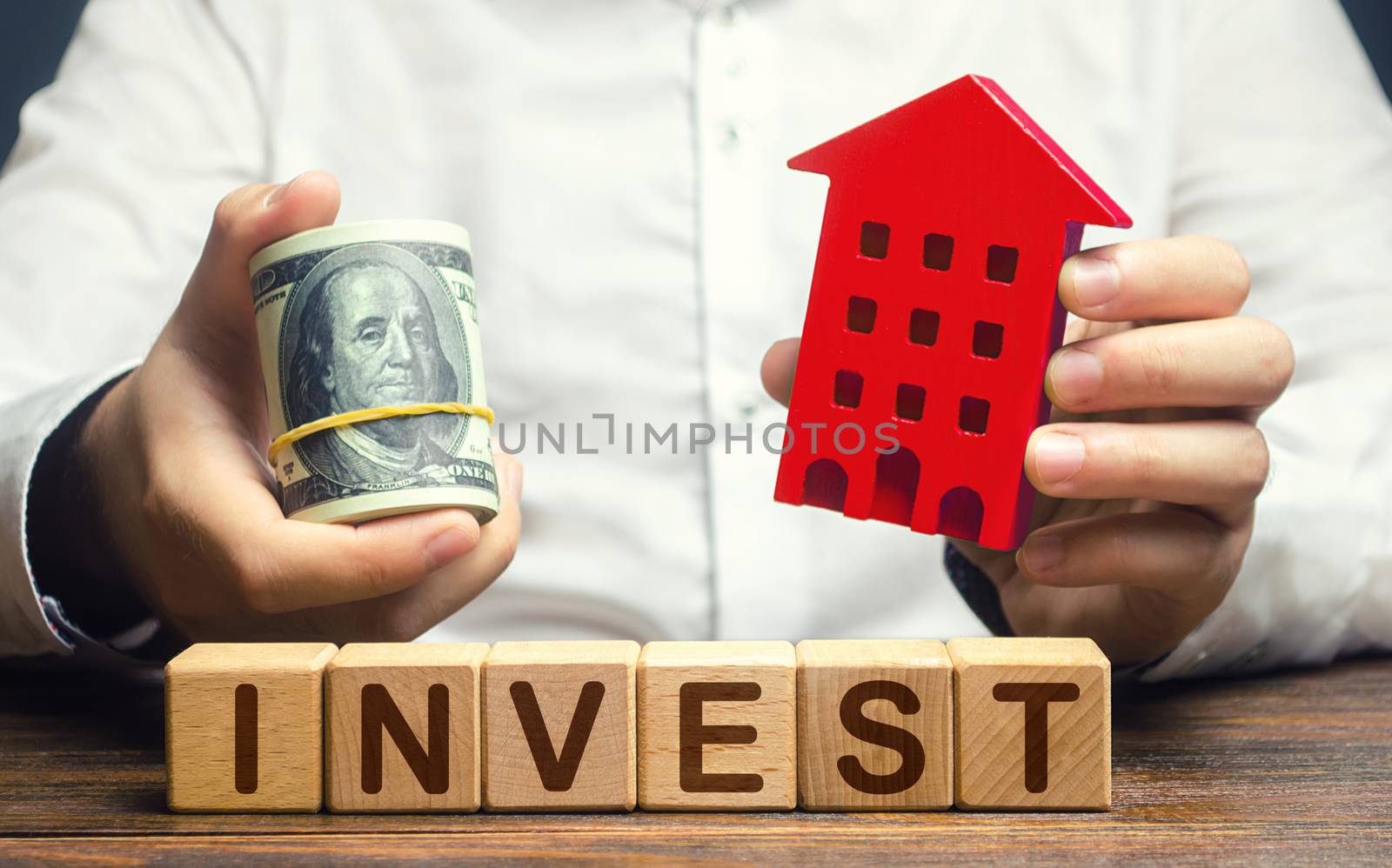 A man with dollars and a house figurine and the word Invest. Real estate financial investment. Favorable investment climate, cheap housing and low demand. Saving savings in a crisis. Rental business