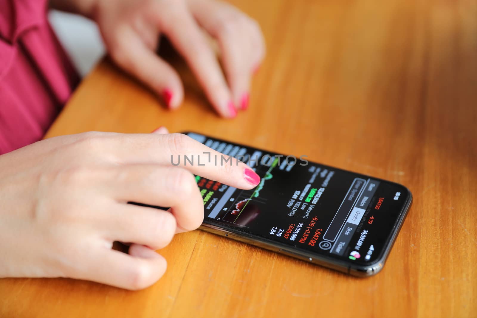 Female hand with smartphone trading stock online in coffee shop  by piyato