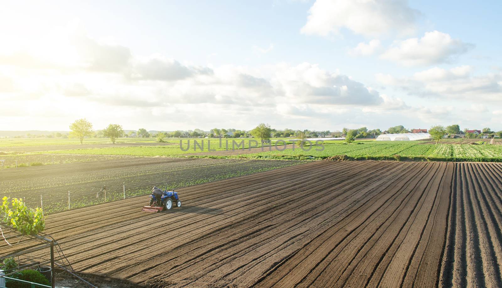 A tractor rides on a farm field. Farmer on a tractor with milling machine loosens, grinds and mixes soil. Loosening the surface, cultivating the land for further planting. Farming and agriculture. by iLixe48