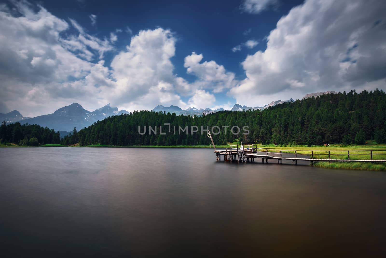 Footbridge over the Lake of Staz near St. Moritz in Switzerland with Swiss Alps in the background. This lake is also known as Stazersee and Lej da Staz. Long exposure.