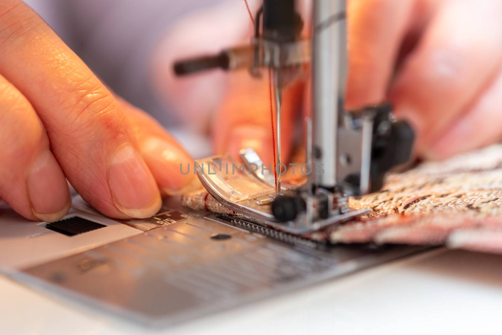 a close-up view of sewing process, hand of old woman using sewing machine, selective focus technique.