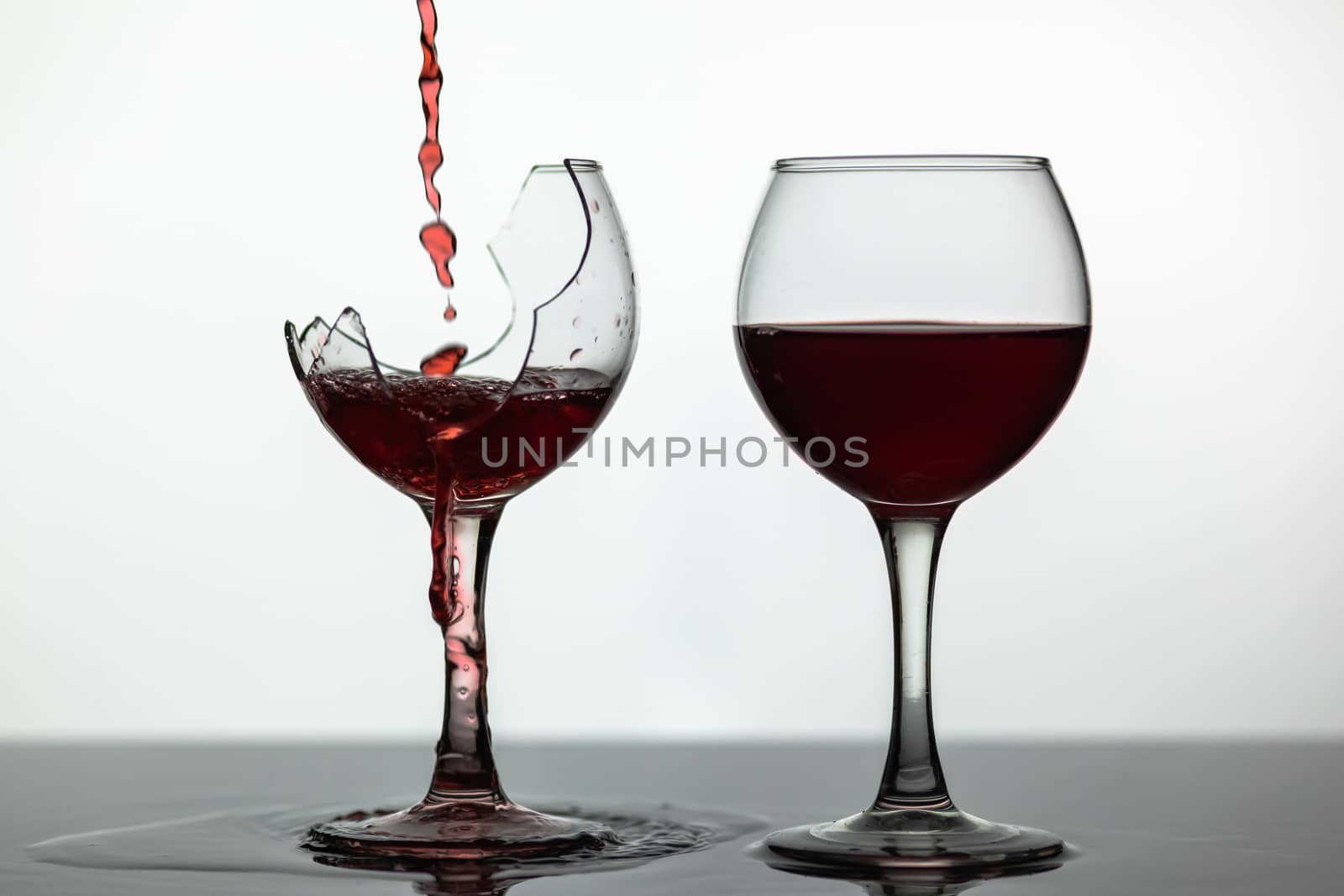 Wine. Red wine pouring into broken wine glass on the wet surface. Rose wine pour. Close up shot. White background