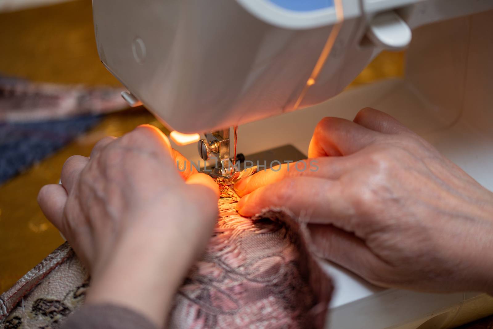 a close-up view of sewing process, hand of old woman using sewing machine, selective focus technique.