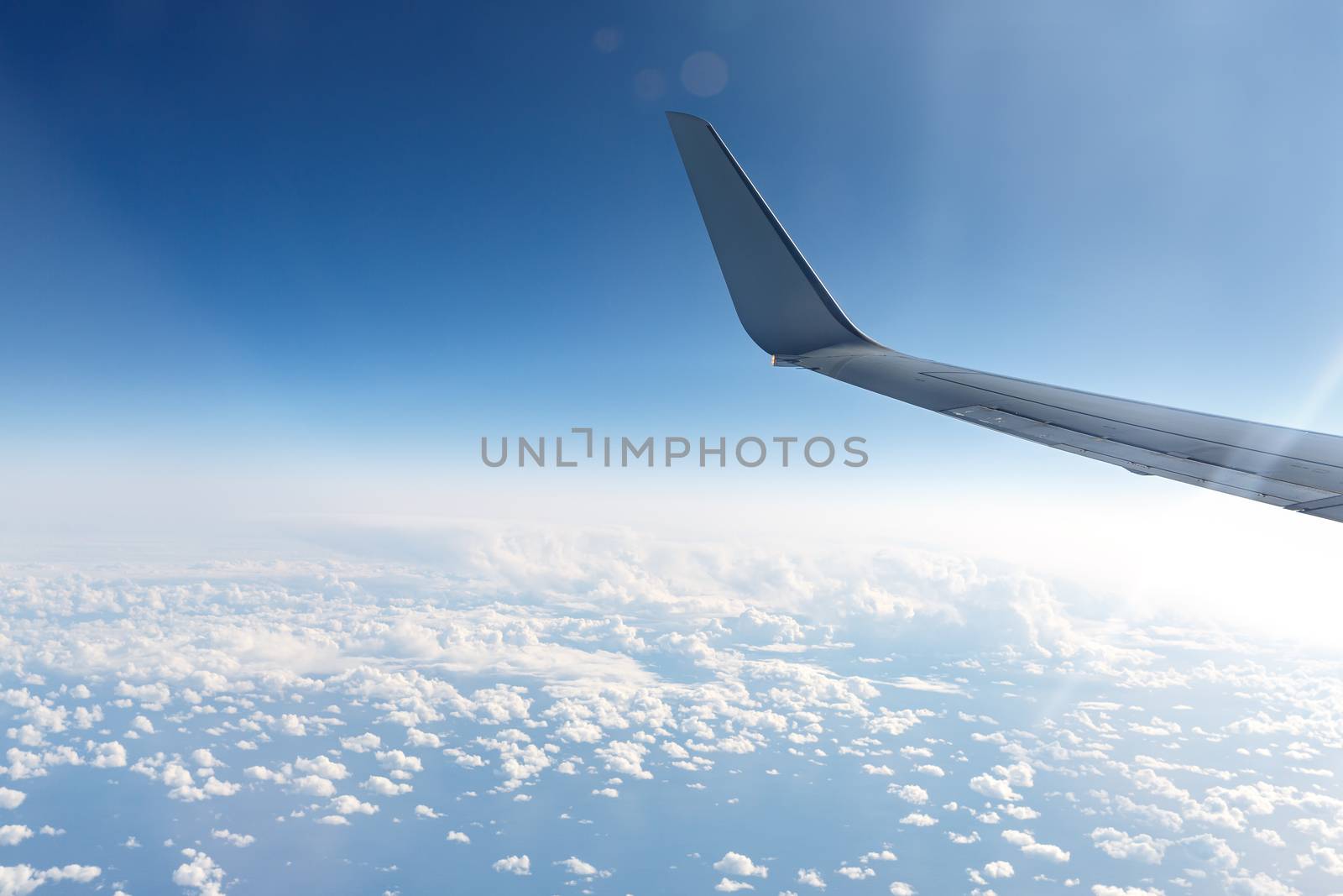 Wing of an airplane in the sky above the blue clouds. by 9parusnikov