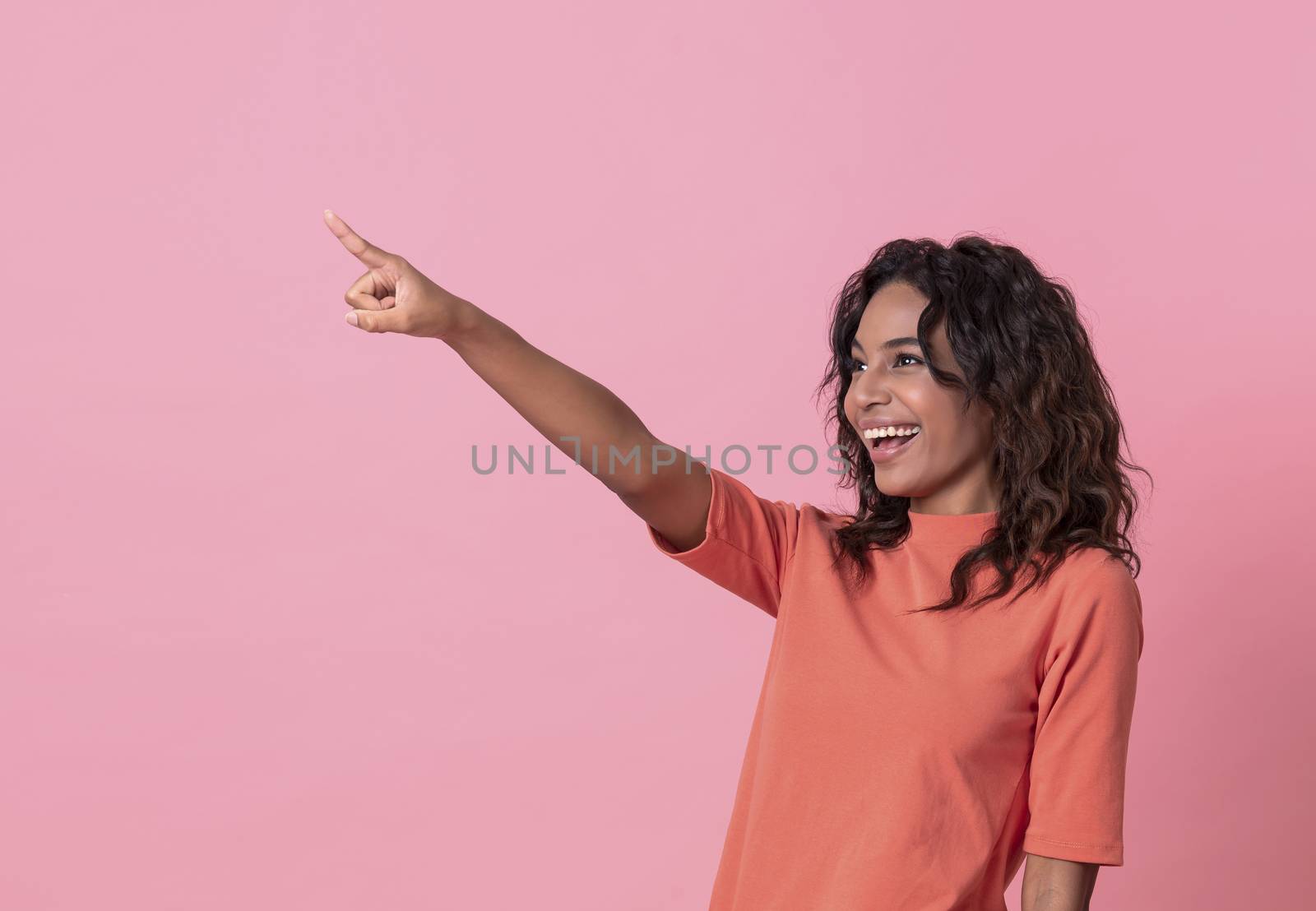 Happy young woman her pointing hand over pink banner background with copy space.
