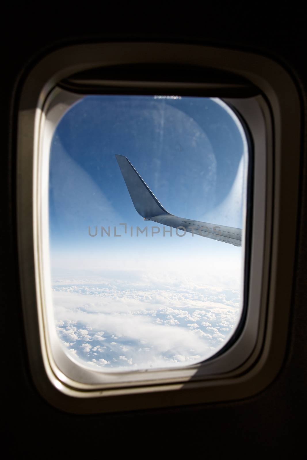 Wing of an airplane above the blue clouds in porthole