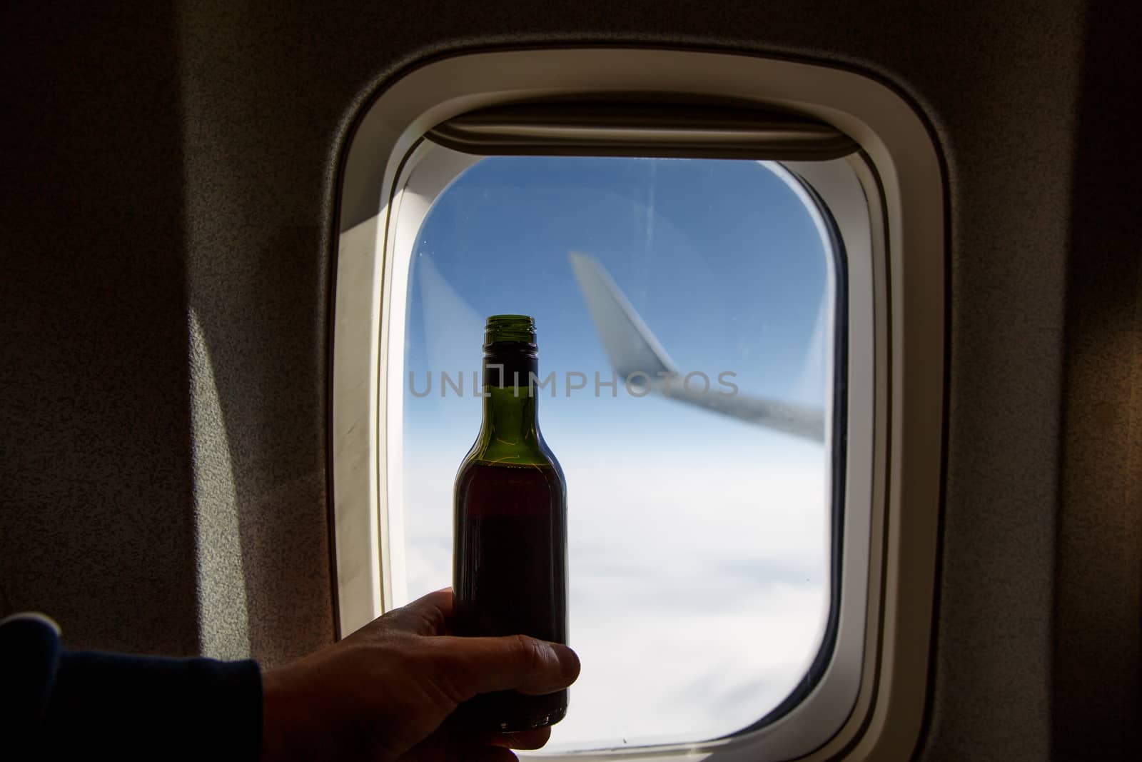 A bottle of wine opposite the porthole. Alcohol on board an airplane. by 9parusnikov