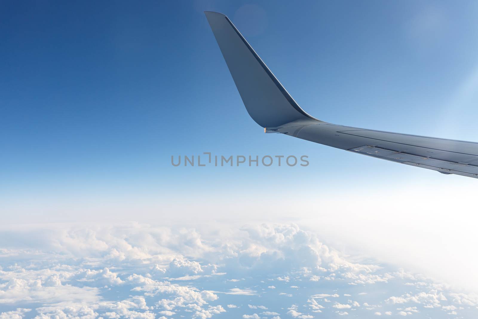 Wing of an airplane in the sky above the blue clouds. by 9parusnikov