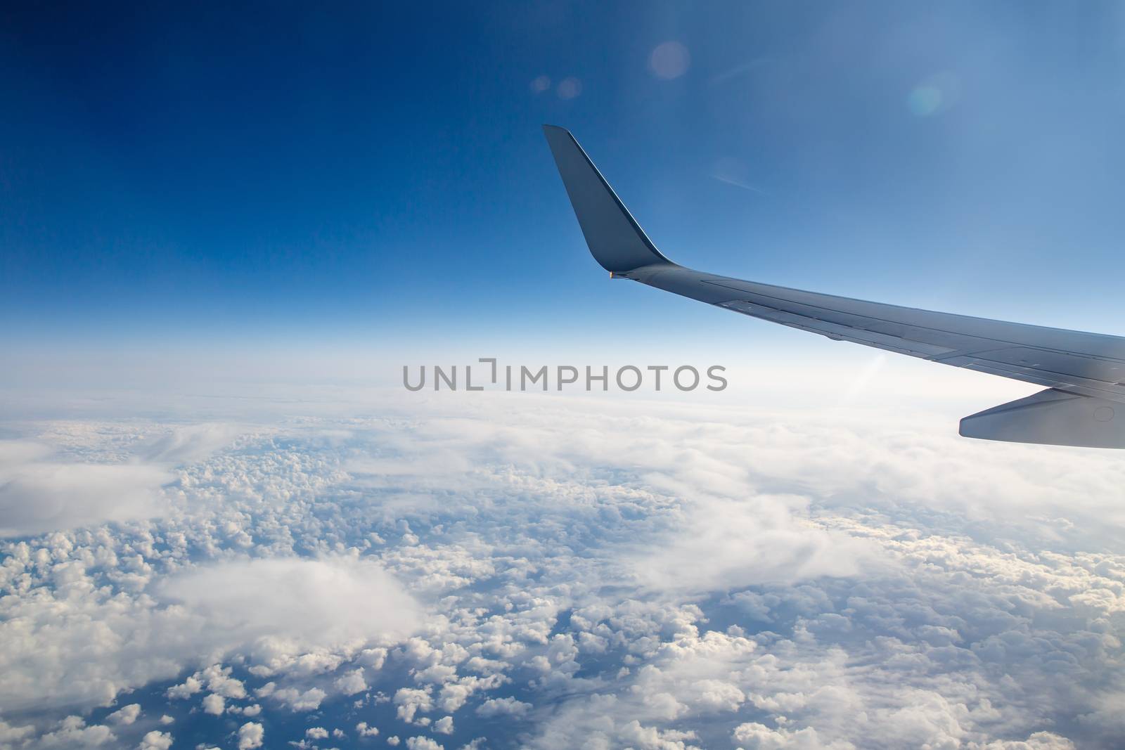 Wing of an airplane in the sky above the blue clouds. by 9parusnikov