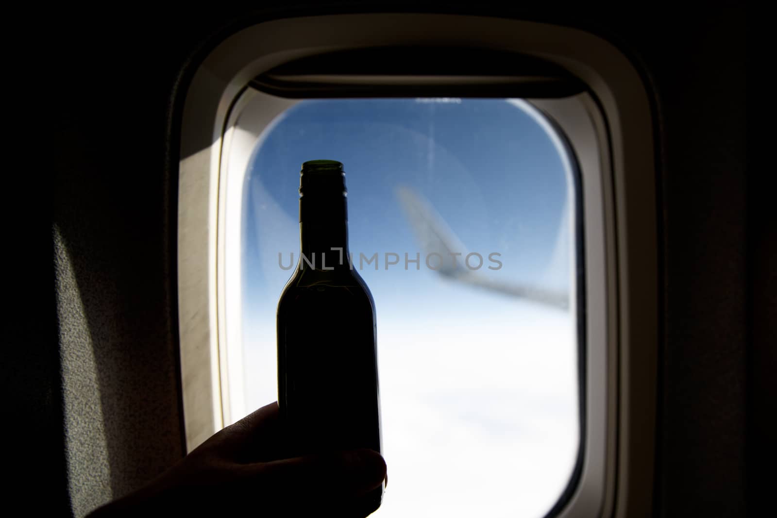 A bottle of wine opposite the porthole. Alcohol on board an airplane. by 9parusnikov