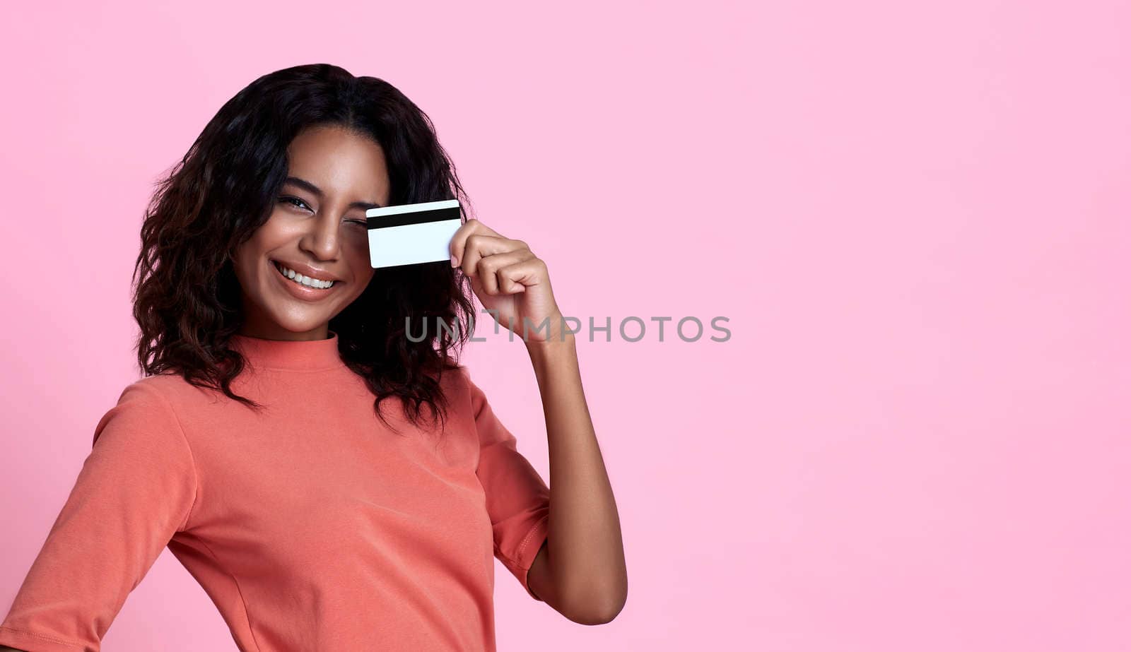 Young smiling beautiful african woman showing credit card in hand over pink banner background with copy space.