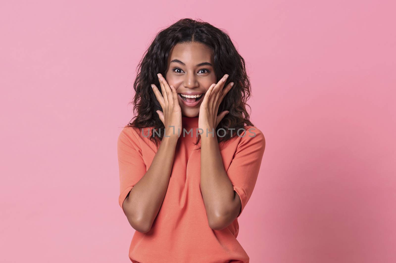 Shocked excited beautiful african woman with mouth open wearing casual orange t-shirt isolated on pink background.