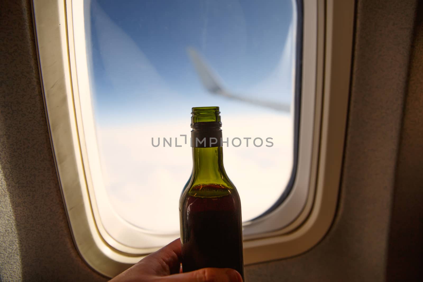 A bottle of wine opposite the porthole. Alcohol on board an airplane. by 9parusnikov