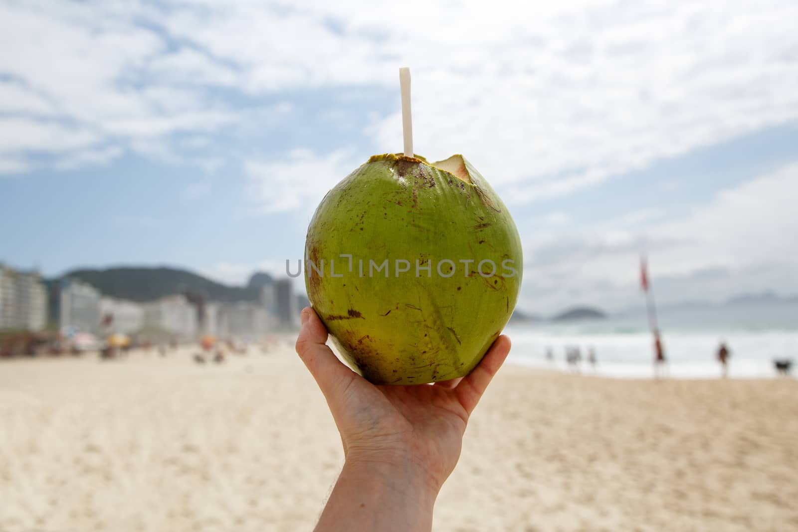 Fresh green coconut with a straw on a beach background. by 9parusnikov