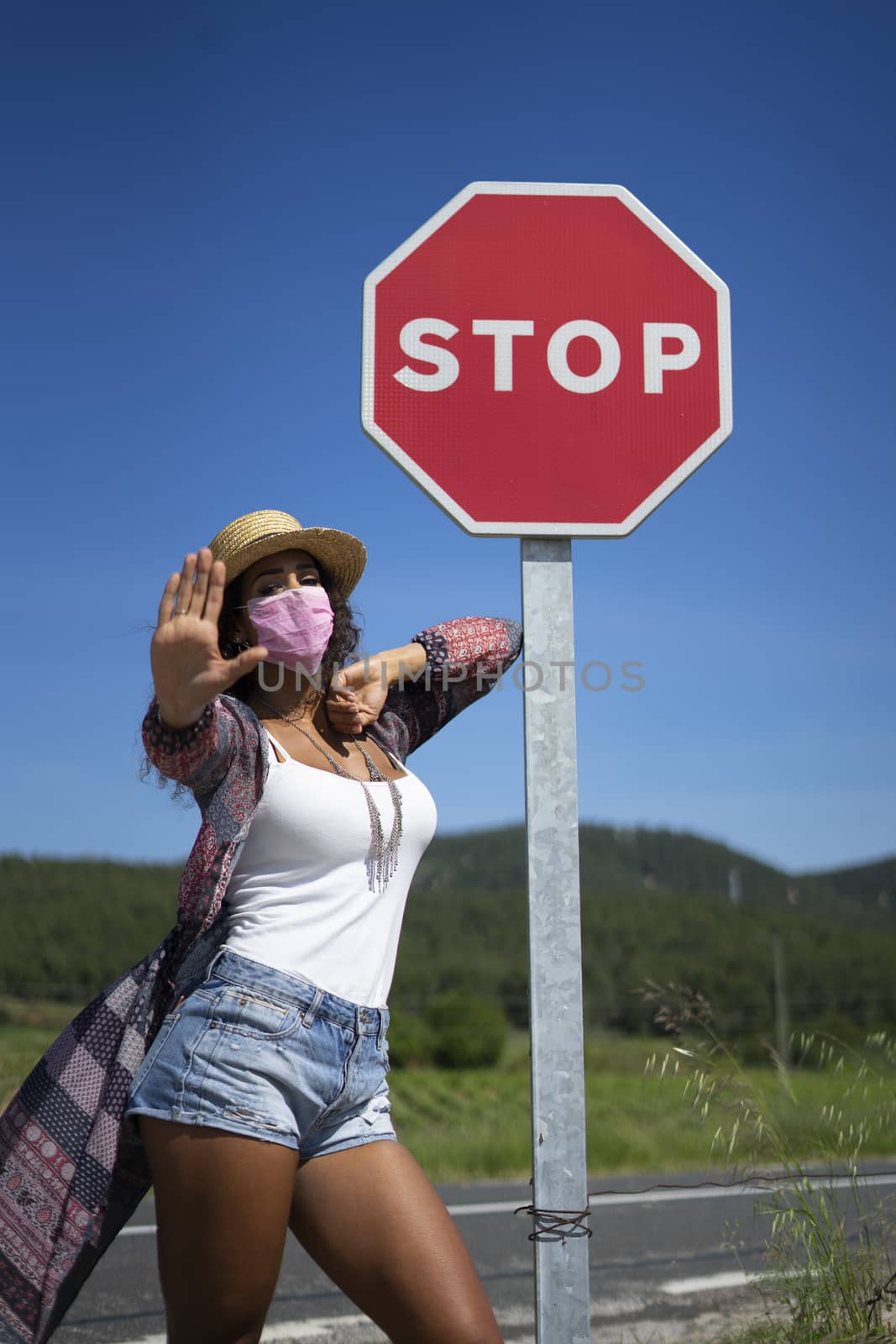 Portrait of a pretty young Brazilian woman looking at the camera with a mask protection for coronavirus infection and a stop sign