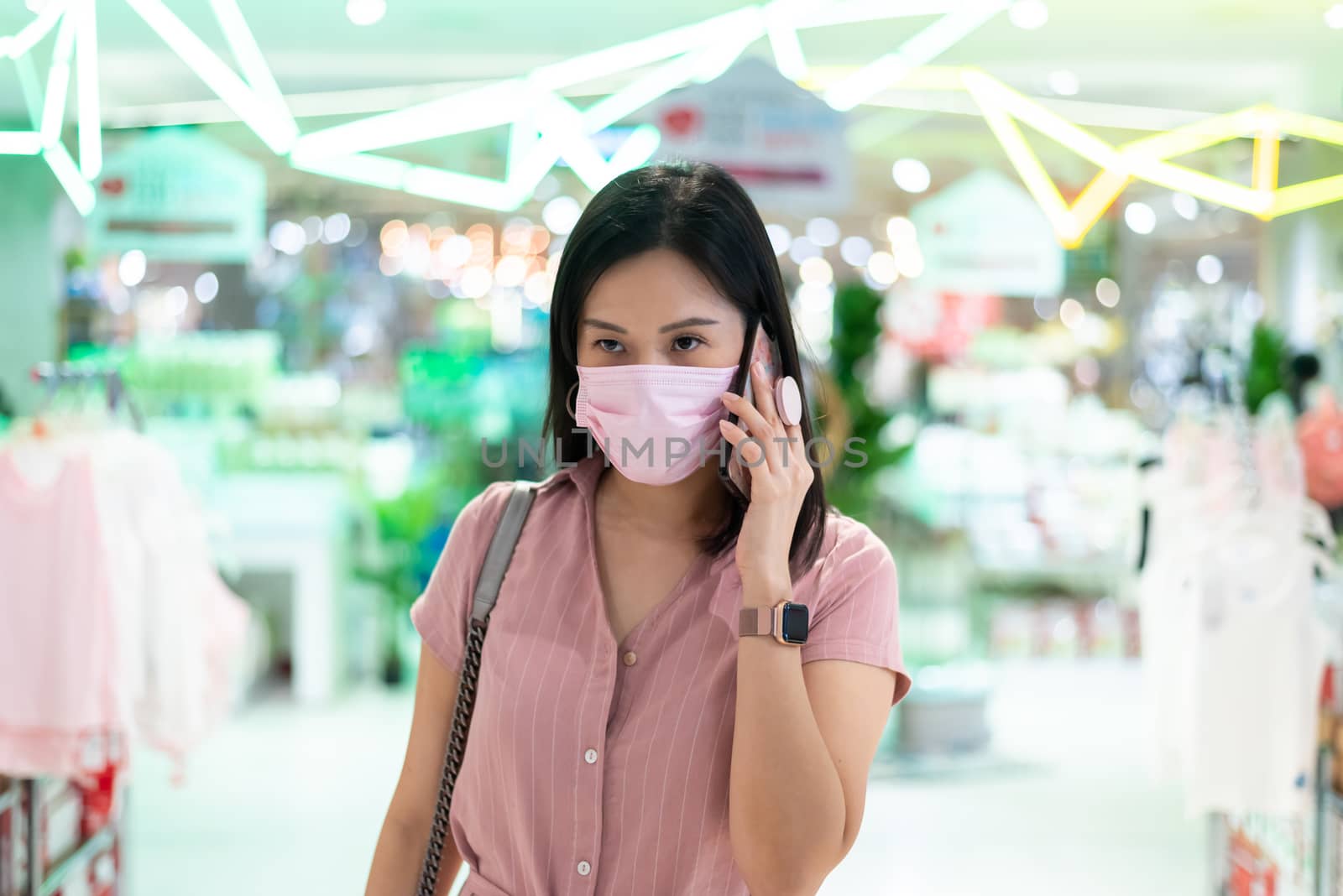 An Asian woman talking and shopping in the shopping mall after opening lockdown with pink mask and social distancing.
