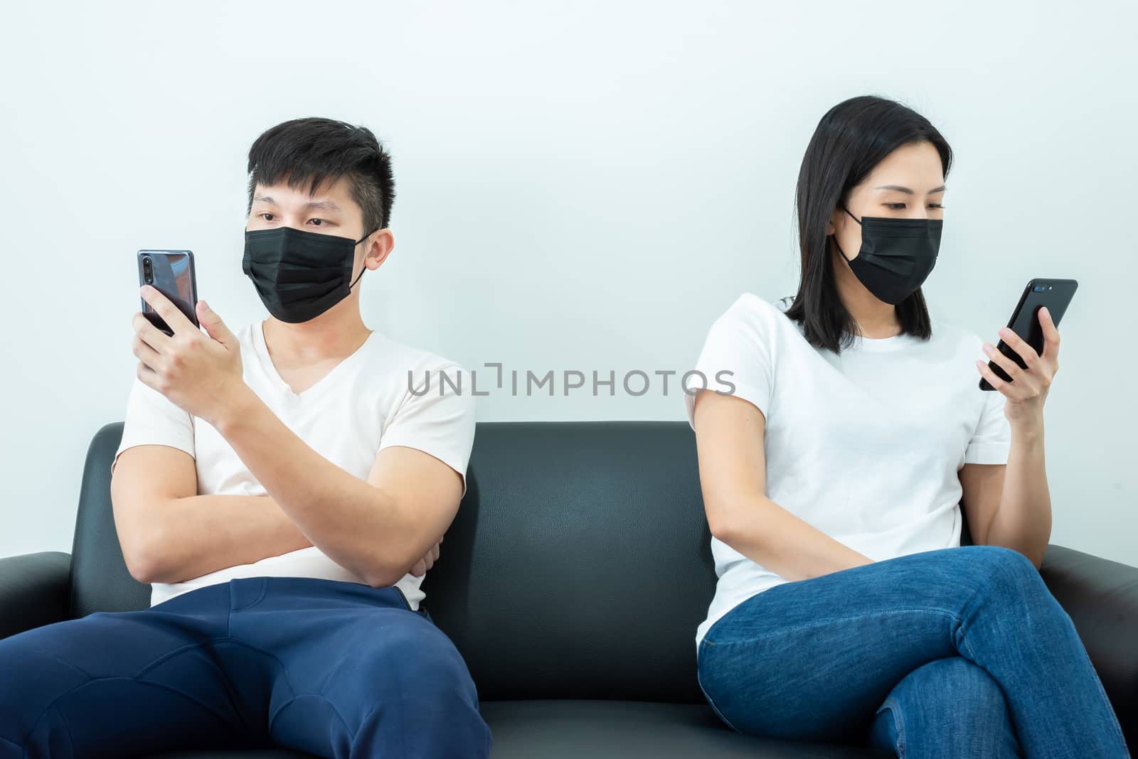 An Asian couple stays together and playing the phone with black mask and social distancing.