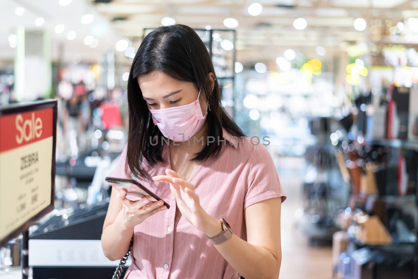 An Asian woman shopping in the shopping mall after opening lockdown with pink mask and social distancing.