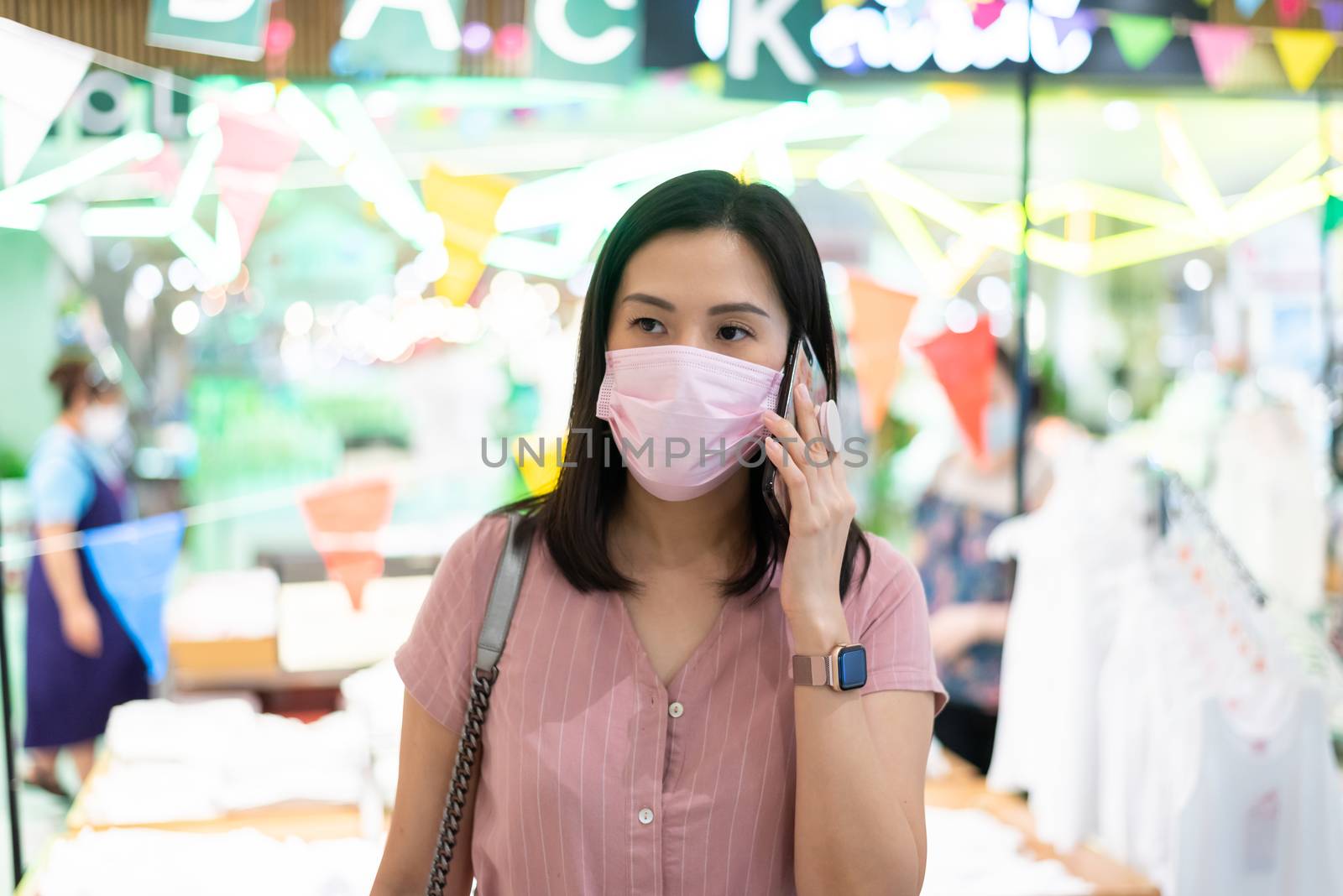 An Asian woman talking and shopping in the shopping mall after opening lockdown with pink mask and social distancing.