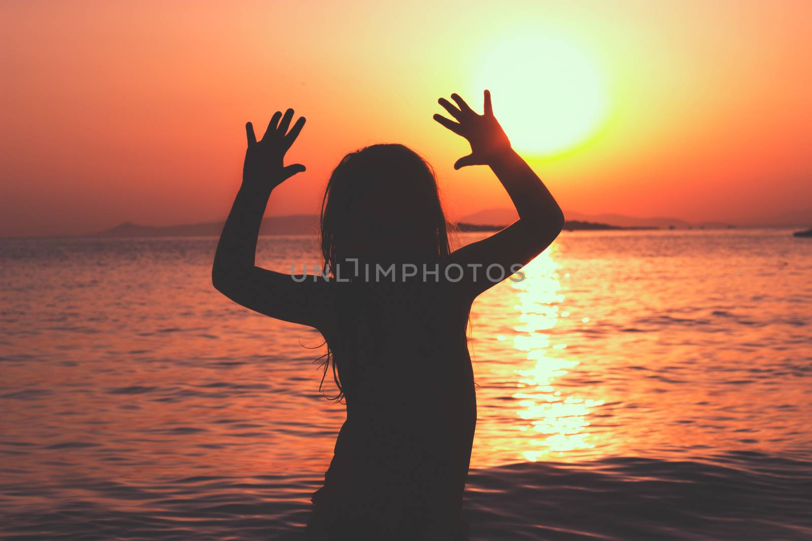 Silhouette of a little girl on the beach, sunset behind her