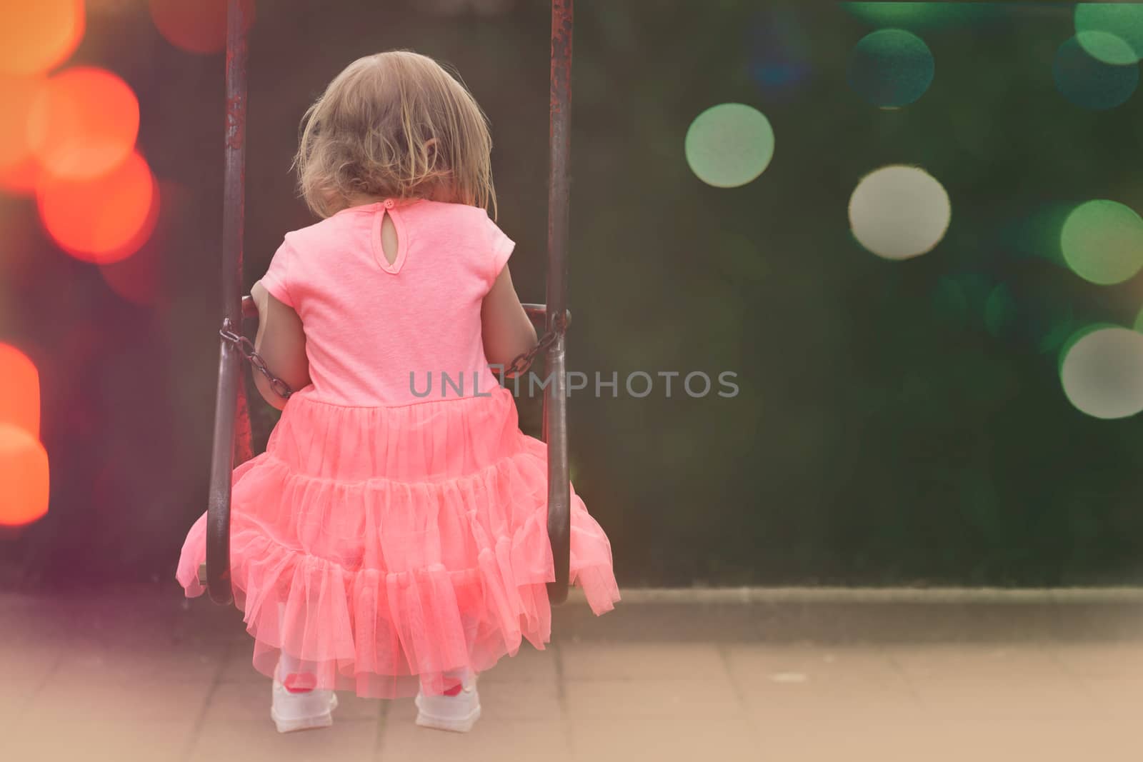 Little girl in beautiful pink dress swinging