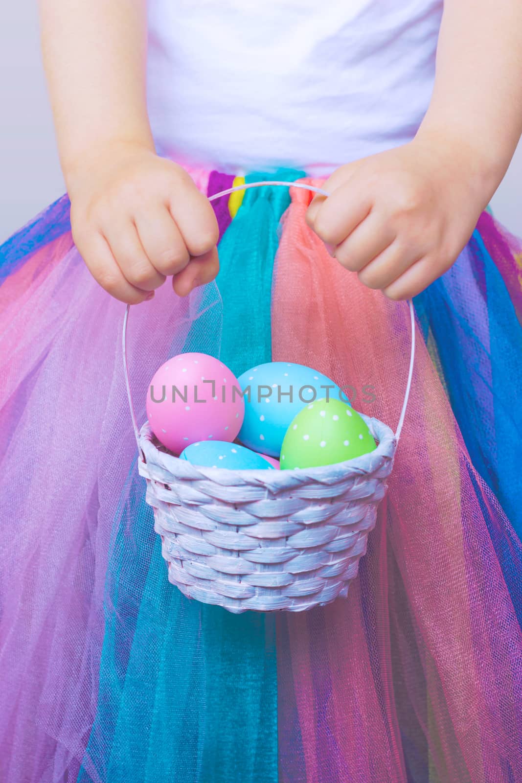 Little girl in tutu skirt, holding colorful easter egg in the basket