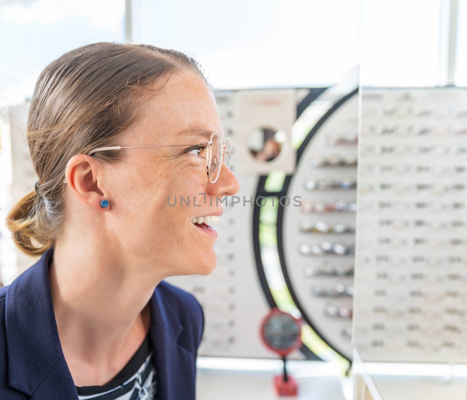 business woman tries glasses in front of a mirror in an optics store by Edophoto