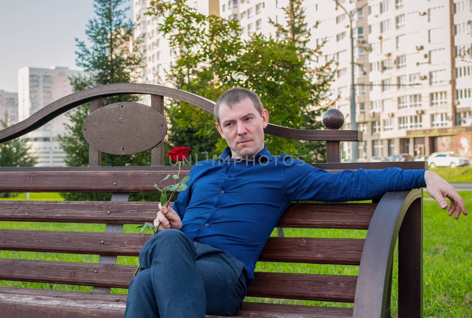 Sad man sitting on a park bench with a rose in his hands and thinking about something