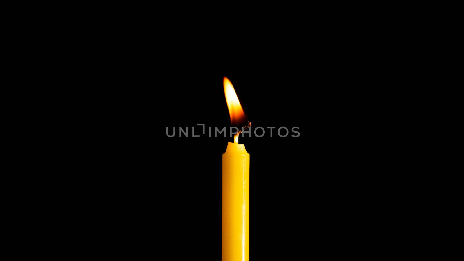 Close-up of a yellow candle illuminated in a black background.